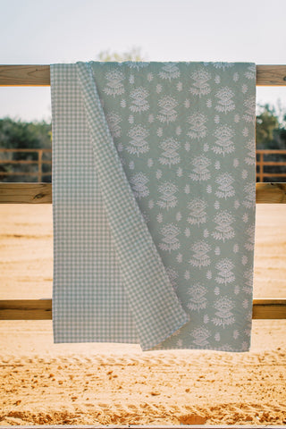 Reversible sage green quilt with floral block print and gingham check pattern draped over wooden fence rail