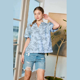 Woman wearing a blue floral blouse and denim shorts indoors.