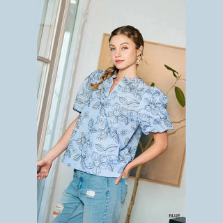 Woman wearing a light blue floral blouse and jeans indoors.