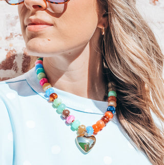Colorful beaded necklace with gold heart pendant worn by model outdoors