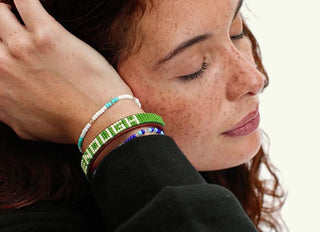 Woman wearing green beaded leather bracelet spelling ENOUGH on wrist near face