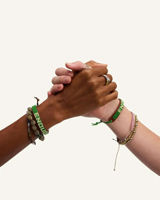 Two hands clasped together each wearing matching green beaded leather bracelets with stacked accessories.