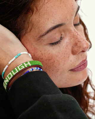 Woman with freckles wearing green beaded leather bracelet spelling ENOUGH on wrist.