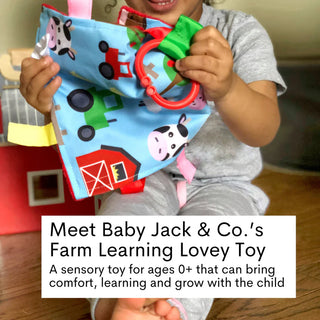Baby gripping red ring on blue farm learning lovey with cow pig tractor print