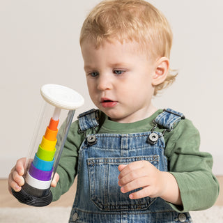 Toddler in denim overalls holding and examining the Fat Brain Toys Flipty rainbow stacking tube toy