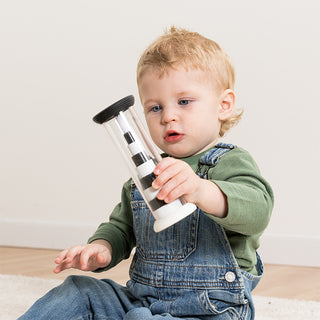 Toddler in denim overalls holding Fat Brain Toys Flipty black and white cylinder toy