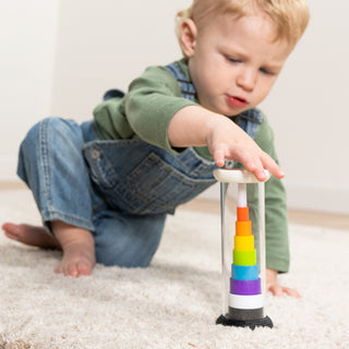 Toddler boy reaching toward Fat Brain Toys Flipty rainbow stacking tower on carpet