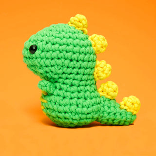 Woobles Fred the Dinosaur crochet amigurumi toy in green with yellow spines on orange background