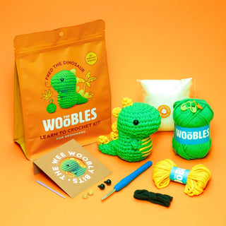 Woobles Fred the Dinosaur beginner crochet kit with green yarn, hook, and finished amigurumi dinosaur