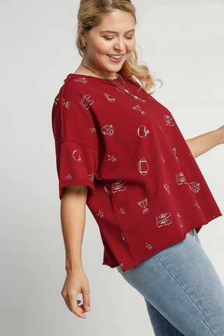 Woman wearing wine-colored French terry oversized top with white football-themed print pattern and jeans