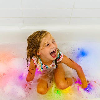 Child laughing joyfully in bathtub with colorful Glo Pals light-up cubes glowing in water