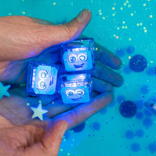 Hand holding three glowing blue Glo Pals Blair light-up sensory cubes with smiley faces