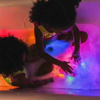 Two children playing with glowing Glo Pals light-up cubes in a bubble bath with colorful LED lights