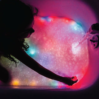 Child placing Glo Pals light-up cubes in a bubble bath with colorful glowing water