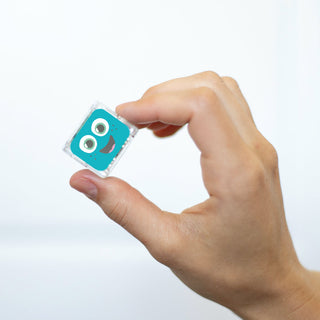 Hand holding a small teal Glo Pals Blair light-up cube with smiling face character