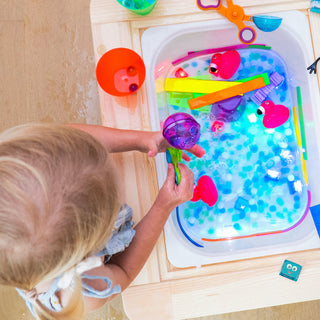 Young child playing with Glo Pals Blair light-up cubes in a water sensory bin with colorful toys.
