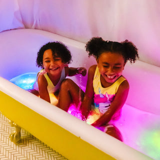 Two happy children sitting in a bathtub with colorful Glo Pals light-up cubes glowing in water