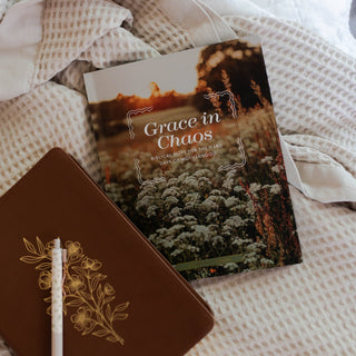 Grace in Chaos Bible study book beside a brown floral journal on white bedding