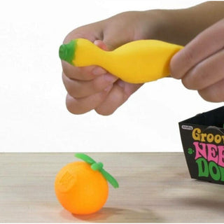 Hand holding a yellow stress ball with green stem, next to an orange stress ball with green stem on a wooden surface.