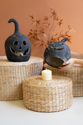 Dark blue clay jack-o'-lanterns with carved faces displayed on woven baskets with candle