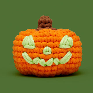 Crocheted orange jack-o-lantern with light green embroidered face and brown stem