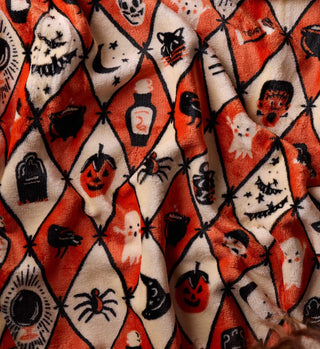 Close-up detail of Halloween argyle fleece blanket with orange and cream diamond pattern featuring spooky icons