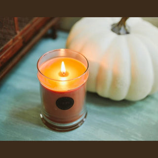 Lit Harvest Pumpkin candle with steady flame on teal wood next to ribbed white pumpkin