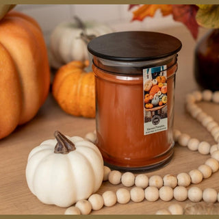 Harvest Pumpkin 8oz jar candle with amber wax and black lid styled with ceramic pumpkin and autumn leaves