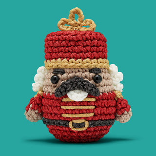 Crocheted nutcracker amigurumi ornament in red uniform with gold accents and black mustache