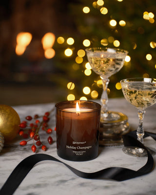 Aromatique Holiday Champagne 10oz fragranced candle glowing warmly amid holiday champagne coupes and festive decor