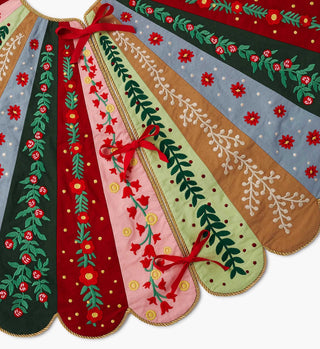 Close-up detail of Holly Jolly embroidered Christmas tree skirt panels with floral motifs and red ribbon ties