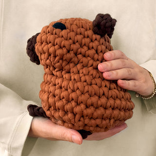 Hands holding a chunky crocheted capybara plush toy in rust brown with dark brown accents