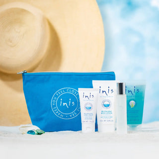 Inis Voyager Gift Set with blue cosmetic bag, hand cream, body lotion, cologne, and shower gel on sandy surface.