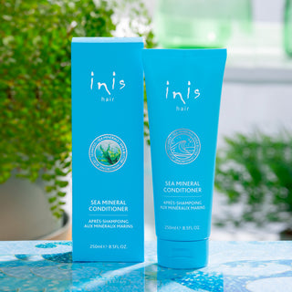 Two blue bottles of 'inis hair' sea mineral conditioner on a table with a blurred green background.