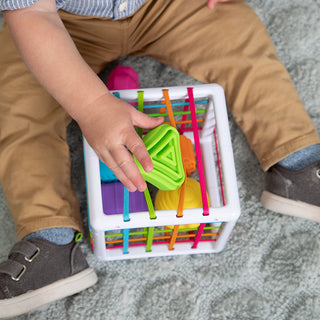 Toddler placing a green triangle shape into the colorful Fat Brain Toys InnyBin sorting toy