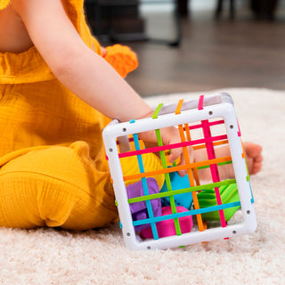 Baby playing with Fat Brain Toys InnyBin colorful elastic band sensory activity cube toy