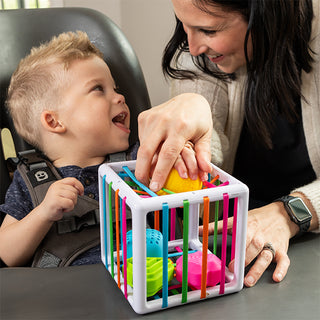 Adult helping toddler play with Fat Brain Toys InnyBin colorful shape-sorting cube toy