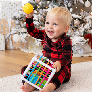Baby smiling and holding Fat Brain Toys InnyBin shape sorter toy near Christmas tree