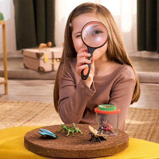 Child using magnifying glass to examine Schleich insect toy figures on cork display board