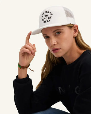 White trucker hat with 'It's Okay To Not Be Okay' embroidered text and mesh back