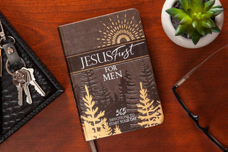 Closed dark brown Jesus First for Men hardcover book with embossed pine trees and gold sunburst on wood