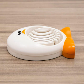 Closed glossy white penguin egg slicer with black eyes and orange beak top view