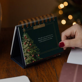 Dark green Christmas advent flipbook Day 9 with gold spiral binding on wooden desk