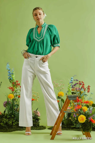 Woman in a green blouse and white pants standing in front of floral arrangements 