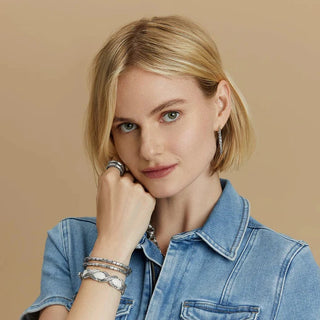 Woman wearing white Kriss Kross Etched Bandit Bracelet with layered silver jewelry and denim shirt
