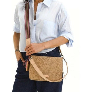 Person holding a beige crossbody bag with intricate patterns