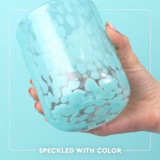 Hand holding a speckled blue glass jar against a light blue background