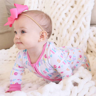 Baby in cozy chunky knit blanket wearing white Little Sister pajama romper with pink bow headband
