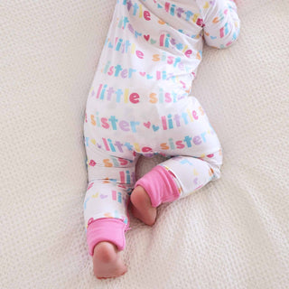 Top-down view of white Little Sister footie romper on crib mattress highlighting side zipper closure