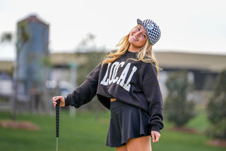 Model wearing black Local Girl Crescent Crew sweatshirt on golf course holding putter